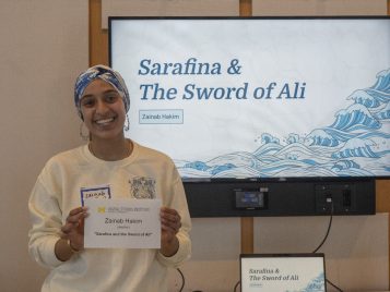 Zainab Hakim stands in front of a large monitor displaying her project.
